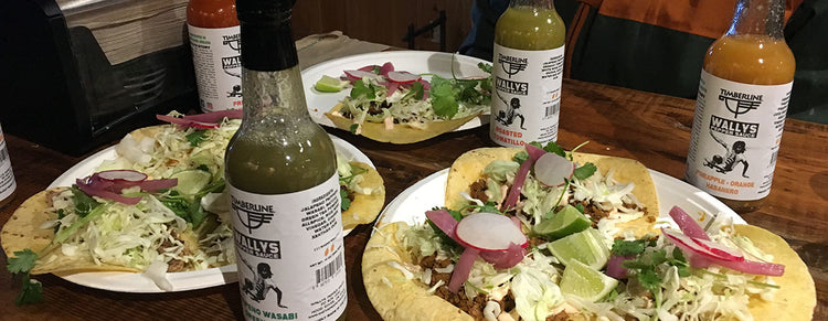 Plates of street tacos with bottles of Wallys Pepper Sauce on the table